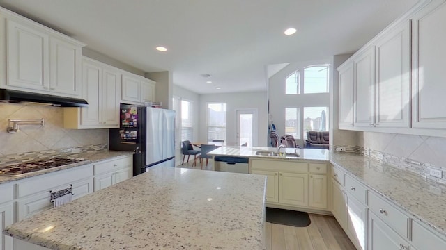 kitchen with stainless steel appliances, light stone countertops, backsplash, and light hardwood / wood-style floors