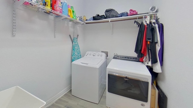 washroom with laundry area, washing machine and clothes dryer, light wood-style flooring, and baseboards