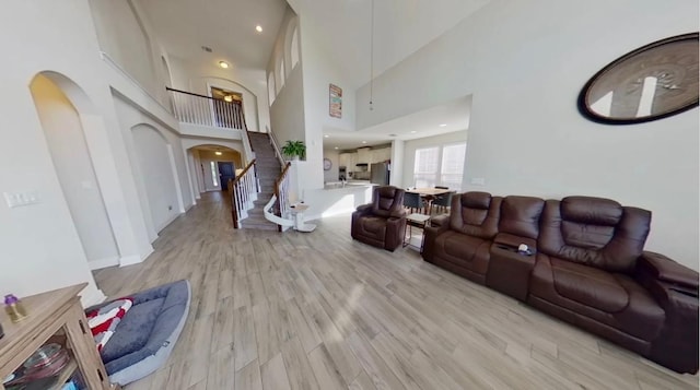 living area featuring arched walkways, recessed lighting, stairway, light wood-style flooring, and a high ceiling