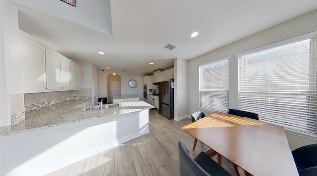 kitchen with light hardwood / wood-style flooring, kitchen peninsula, sink, white cabinetry, and black refrigerator