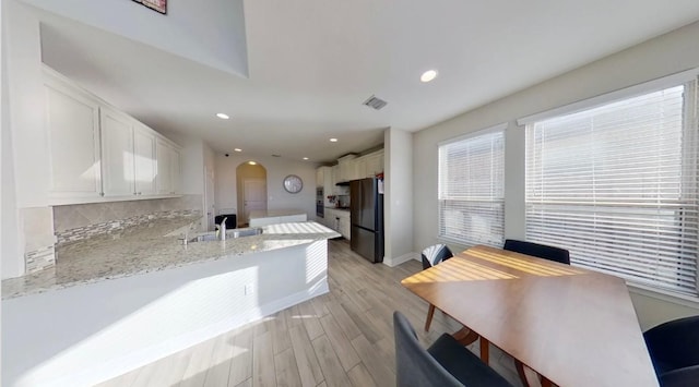 kitchen featuring arched walkways, a peninsula, freestanding refrigerator, and white cabinets