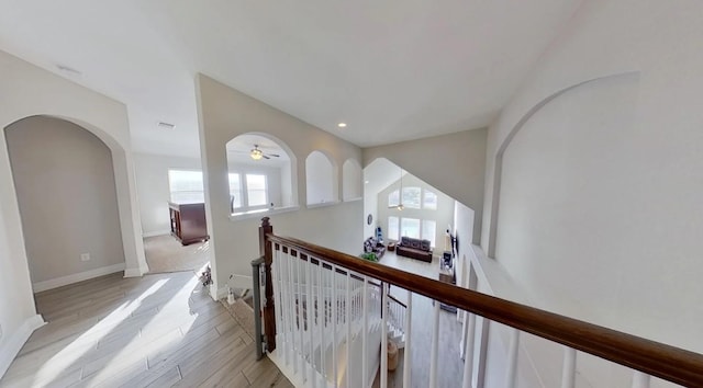 corridor with arched walkways, recessed lighting, an upstairs landing, baseboards, and light wood-type flooring