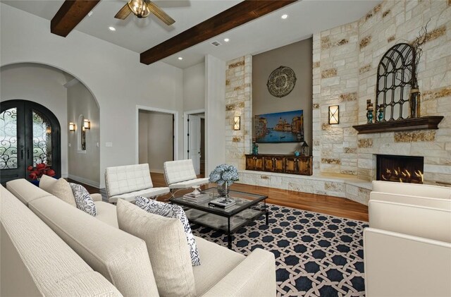 living room with beam ceiling, french doors, a fireplace, wood-type flooring, and ceiling fan