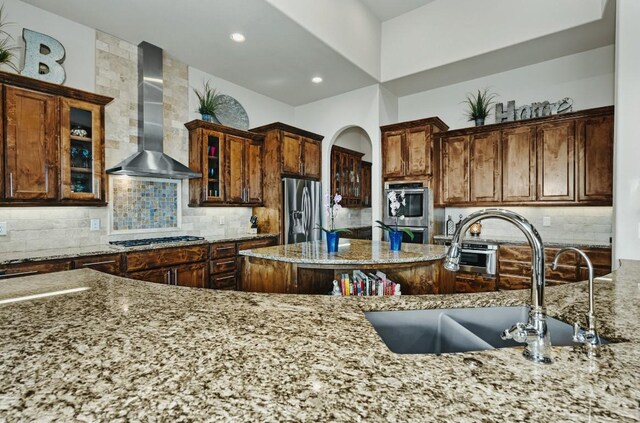 7610 Ramble Rdg, San Antonio, TX 78266 - kitchen with wall chimney range hood, appliances with stainless steel finishes, light stone countertops, glass insert cabinets, and decorative backsplash