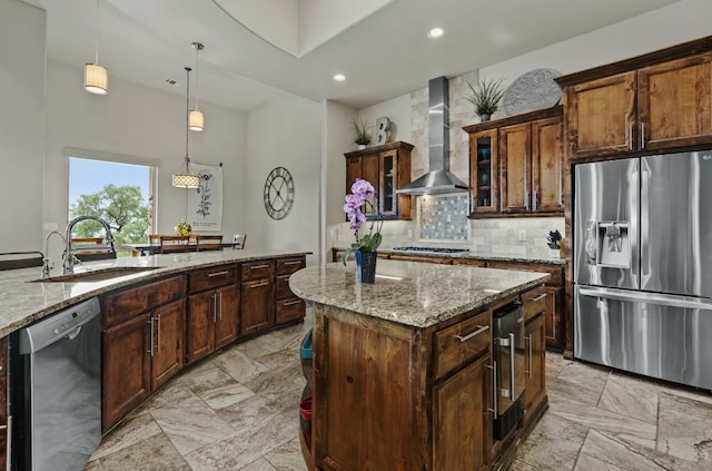 kitchen with wall chimney exhaust hood, appliances with stainless steel finishes, light stone countertops, sink, and a center island