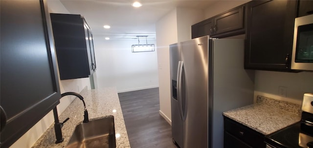 kitchen featuring baseboards, appliances with stainless steel finishes, light stone counters, dark wood-type flooring, and a sink