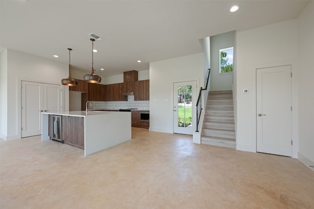 kitchen with decorative light fixtures, tasteful backsplash, beverage cooler, sink, and a center island with sink