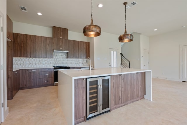 kitchen with tasteful backsplash, beverage cooler, range, sink, and a center island with sink