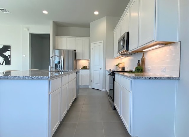 kitchen with white cabinetry, tile patterned floors, an island with sink, decorative backsplash, and appliances with stainless steel finishes