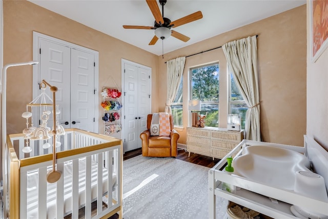 bedroom with a nursery area, hardwood / wood-style floors, and ceiling fan