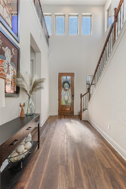 foyer entrance with a wealth of natural light, a towering ceiling, and dark hardwood / wood-style flooring