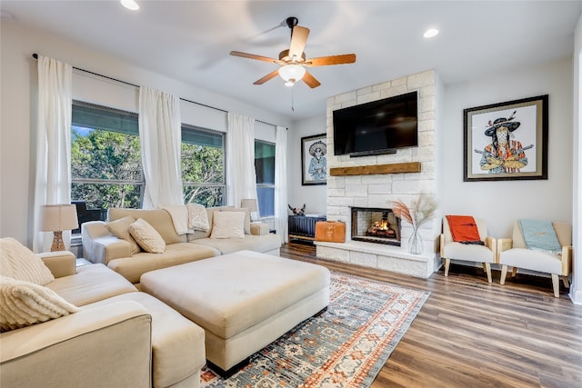 living room featuring hardwood / wood-style flooring, ceiling fan, and a stone fireplace