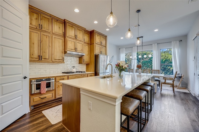 kitchen with a center island with sink, pendant lighting, appliances with stainless steel finishes, and dark hardwood / wood-style floors