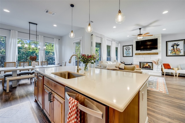 kitchen featuring an island with sink, sink, a stone fireplace, dishwasher, and hardwood / wood-style floors