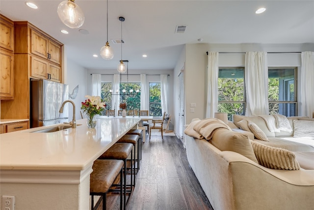 kitchen with stainless steel fridge, dark hardwood / wood-style floors, sink, hanging light fixtures, and a spacious island