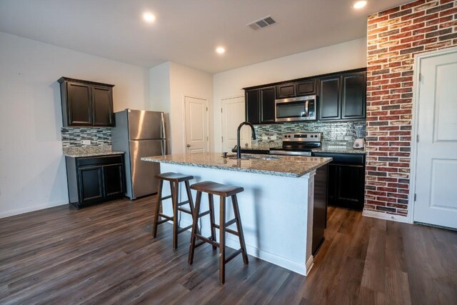 kitchen with appliances with stainless steel finishes, an island with sink, dark wood-type flooring, and sink