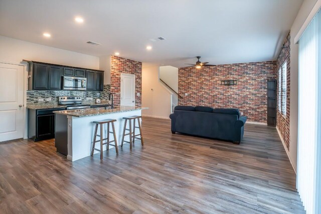 kitchen featuring a kitchen island with sink, dark wood-type flooring, dark stone countertops, a kitchen breakfast bar, and stainless steel appliances