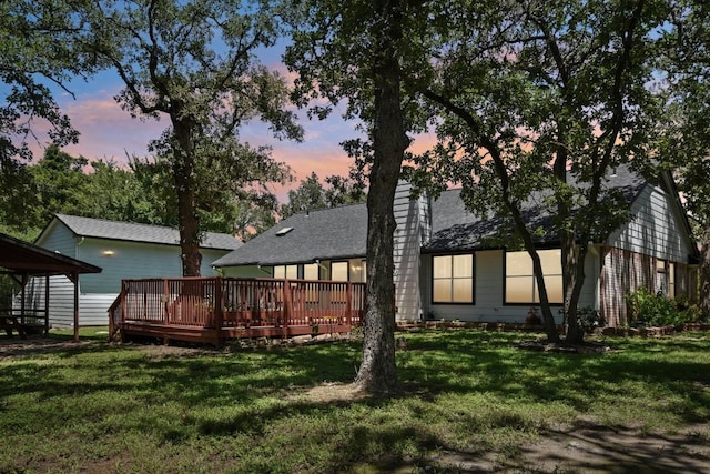 back house at dusk with a wooden deck and a lawn