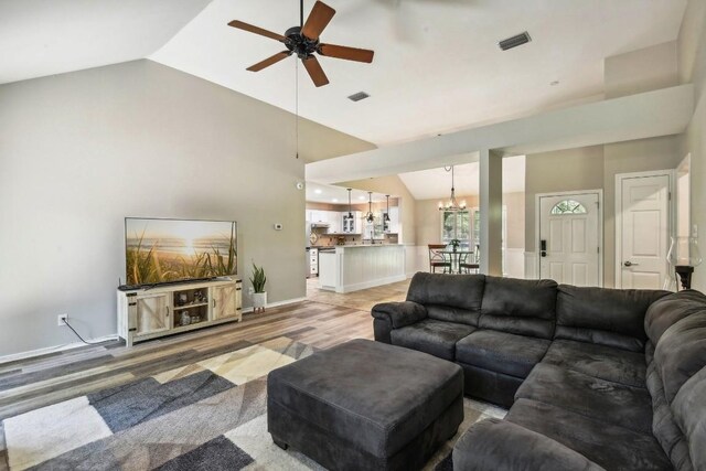 living room with light hardwood / wood-style flooring, ceiling fan with notable chandelier, and high vaulted ceiling