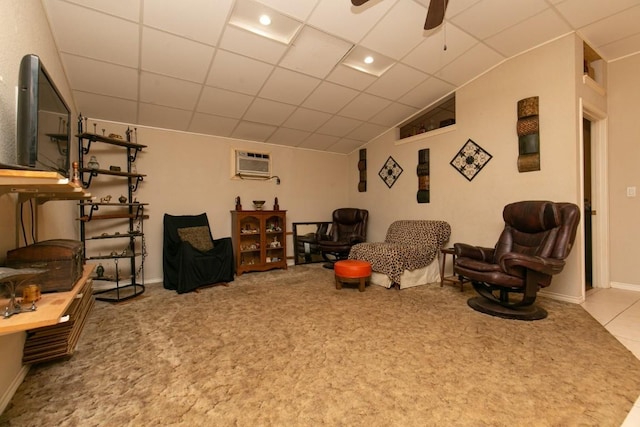 living area with a drop ceiling, light carpet, a ceiling fan, baseboards, and a wall mounted air conditioner