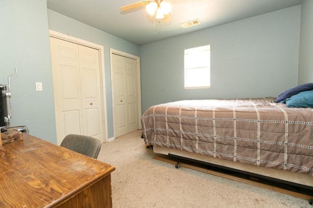 carpeted bedroom featuring a ceiling fan, visible vents, and two closets