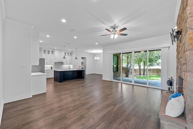 unfurnished living room with ceiling fan with notable chandelier, dark hardwood / wood-style floors, a stone fireplace, sink, and ornamental molding