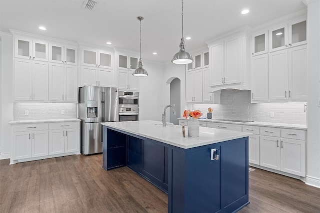 kitchen featuring appliances with stainless steel finishes, a center island with sink, hanging light fixtures, backsplash, and dark wood-type flooring