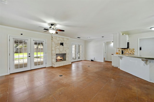 unfurnished living room featuring tile patterned floors, ceiling fan, crown molding, french doors, and a stone fireplace