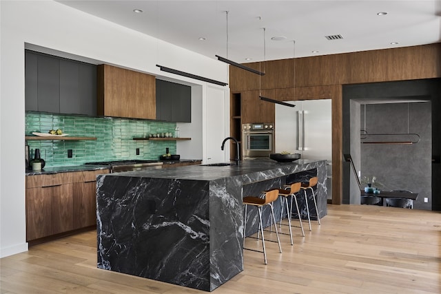 kitchen with sink, light hardwood / wood-style flooring, a barn door, and an island with sink