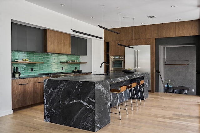 3003 Oakhaven Dr, Austin, TX 78704 - kitchen featuring appliances with stainless steel finishes, modern cabinets, a kitchen bar, light wood-style flooring, and decorative backsplash