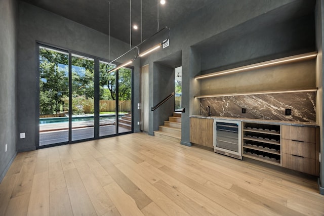 bar with a high ceiling, sink, wine cooler, light hardwood / wood-style flooring, and light stone countertops