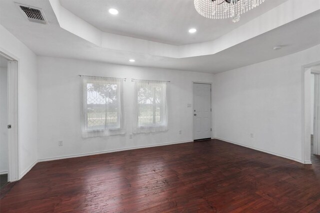 spare room with a notable chandelier, a tray ceiling, and dark wood-type flooring