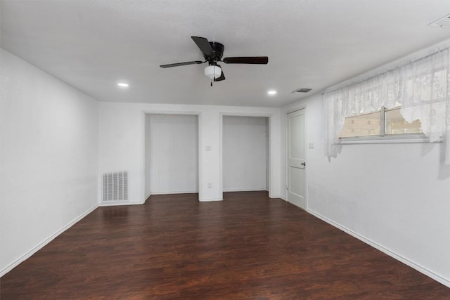 unfurnished bedroom with ceiling fan, dark wood-type flooring, and multiple closets