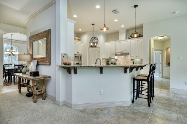 kitchen with white cabinetry, backsplash, light stone counters, decorative light fixtures, and a kitchen bar