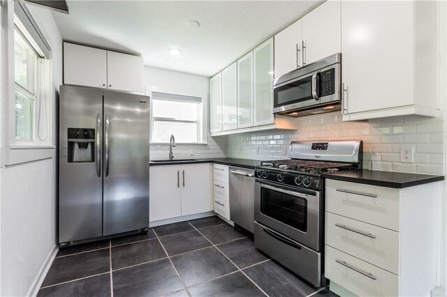 kitchen featuring appliances with stainless steel finishes, tasteful backsplash, dark tile patterned floors, sink, and white cabinetry