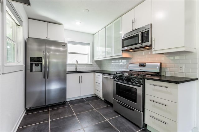 kitchen with dark countertops, decorative backsplash, appliances with stainless steel finishes, white cabinetry, and a sink