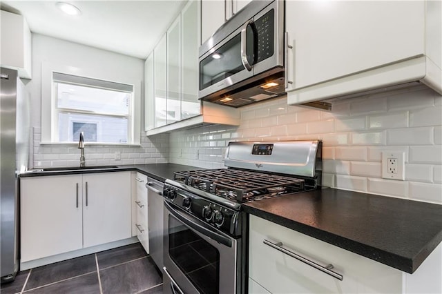 kitchen featuring white cabinets, dark countertops, stainless steel appliances, and a sink