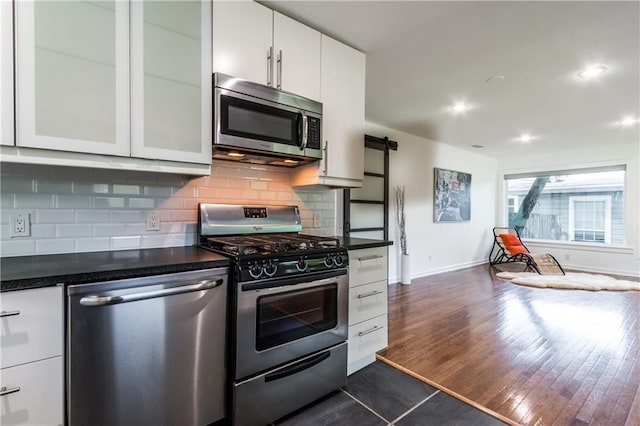 kitchen featuring dark countertops, a barn door, appliances with stainless steel finishes, glass insert cabinets, and white cabinetry