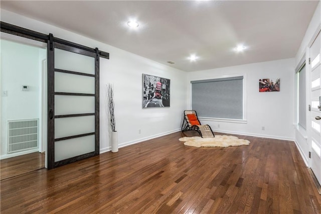 unfurnished room with a barn door, visible vents, dark wood finished floors, and baseboards