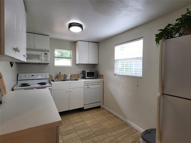 kitchen with white appliances, baseboards, white cabinets, light countertops, and a sink