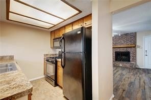 kitchen featuring range, a fireplace, black refrigerator, light wood-type flooring, and brick wall