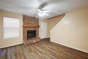 unfurnished living room with hardwood / wood-style flooring, a brick fireplace, brick wall, and ceiling fan