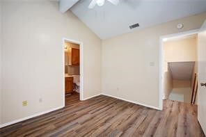 unfurnished bedroom featuring wood-type flooring, vaulted ceiling with beams, ensuite bathroom, and ceiling fan