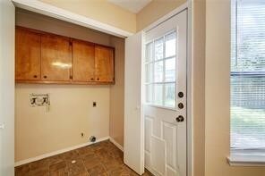 washroom with electric dryer hookup, dark tile patterned floors, and cabinets