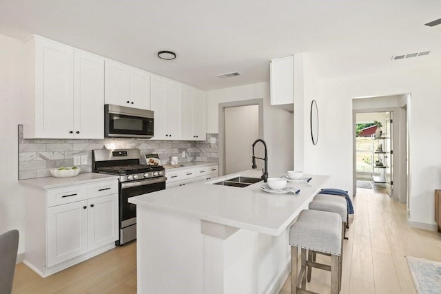 kitchen with decorative backsplash, sink, stainless steel range with gas cooktop, and white cabinetry