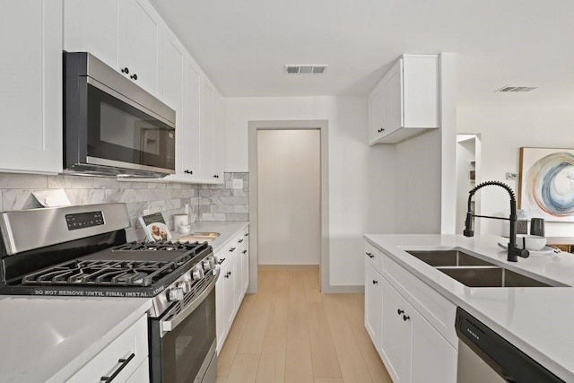 kitchen featuring tasteful backsplash, light wood-type flooring, white cabinets, appliances with stainless steel finishes, and sink