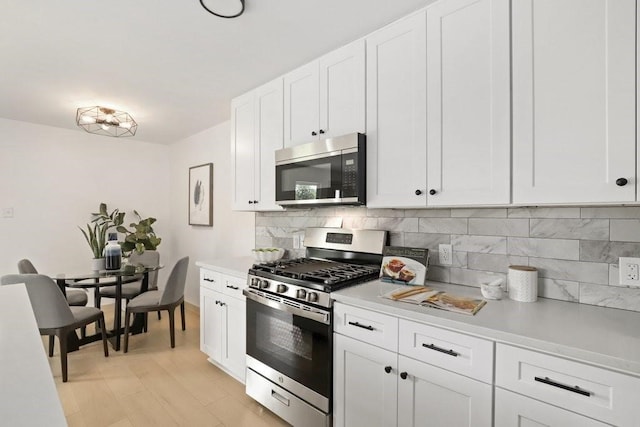 kitchen with appliances with stainless steel finishes, light hardwood / wood-style flooring, white cabinets, and tasteful backsplash