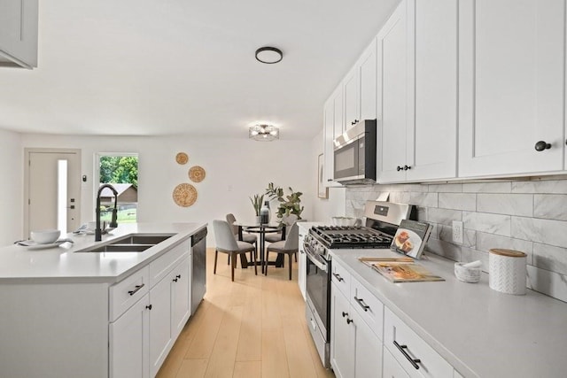 kitchen with tasteful backsplash, white cabinets, light wood-type flooring, sink, and appliances with stainless steel finishes