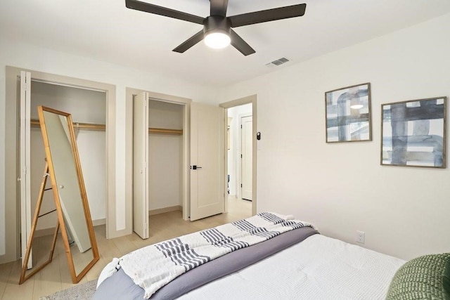 bedroom featuring light hardwood / wood-style floors, two closets, and ceiling fan