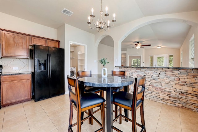 tiled dining space with built in shelves, ceiling fan with notable chandelier, and lofted ceiling